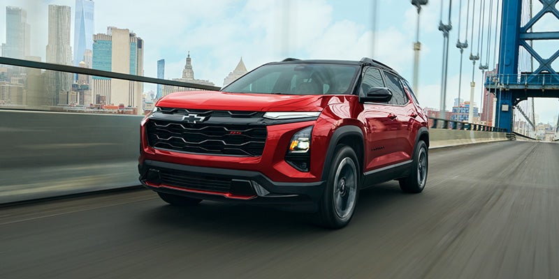 2027 Chevrolet Equinox RS driving across a bridge in Radiant Red Tintcoat